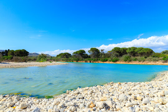 Idyllic tranquil river stream flowing into a tropical sea with a stone beach in summer weather