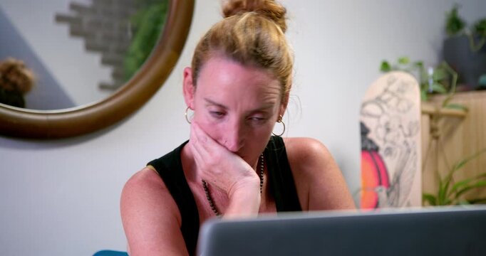 Overwhelmed by Information: A woman with her hand on her chin looks stressed and tired while staring at her laptop screen, indicating information overload or a challenging task.