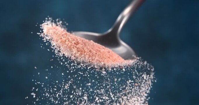 Pink Himalayan salt falling from spoon in slow motion on blue background