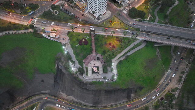 Aerial view of Parque del Amor with its iconic sculpture, lush green gardens, and coastal cliffs, overlooking the highway in Miraflores, Provincia de Lima, Peru.