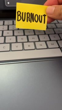 Hand holding burnout sticky note over laptop keyboard