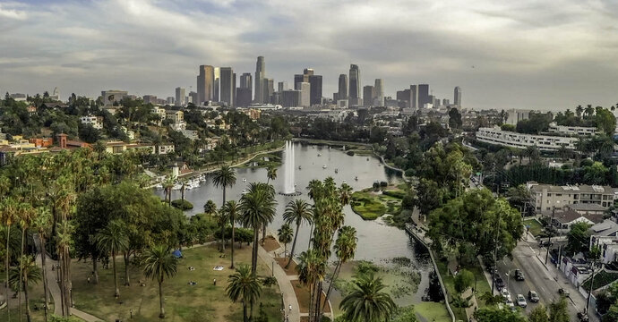 Aerial view of Echo Park Lake with its fountain, surrounded by palm trees and greenery, with the downtown Los Angeles skyline in the distance, Los Angeles, CA, United States.
