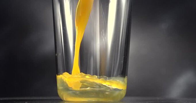 Orange juice pouring into glass in slow motion on black background