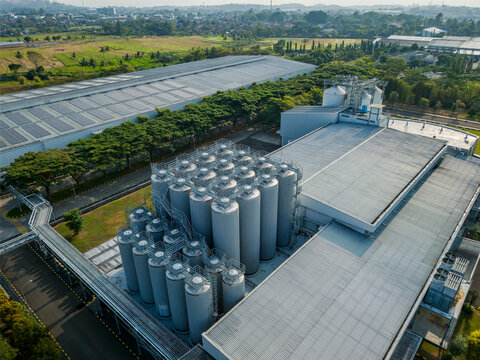 Aerial view of an industrial facility with metal silos, warehouses with solar panels, and surrounding green landscape in Semarang Regency, Central Java, Indonesia.