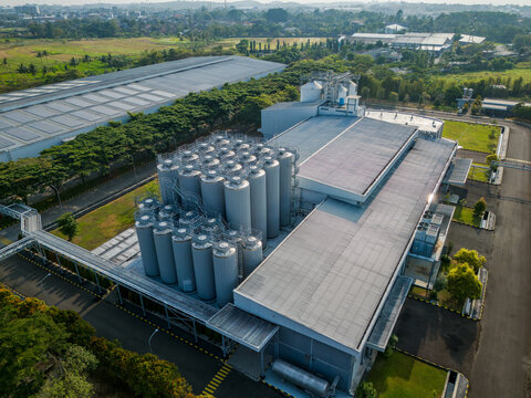 Aerial view of an industrial facility featuring a cluster of large metal storage silos and a modern factory building surrounded by green fields in Semarang Regency, Central Java, Indonesia.