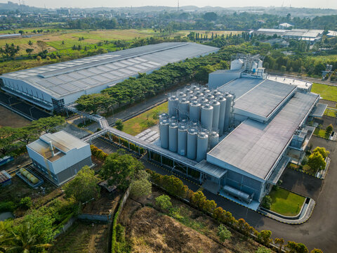 Aerial view of a large industrial facility featuring numerous metal storage silos and a warehouse complex surrounded by green fields in Semarang Regency, Central Java, Indonesia.