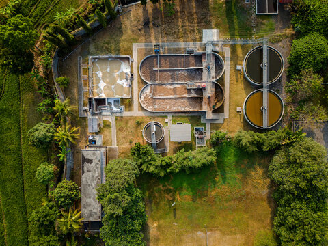 Aerial view of a wastewater treatment plant with circular tanks and aeration basins surrounded by lush vegetation and rice fields in Semarang Regency, Central Java, Indonesia.
