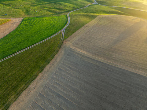 Aerial view of patchwork fields and winding rural roads at golden hour in Fribourg canton, Switzerland.