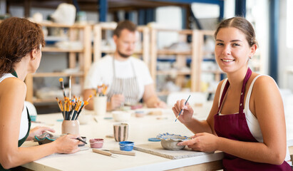 Pottery workers paint ceramic plates together at a table