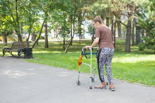 A young woman with cerebral palsy walks in a park with a walker.
