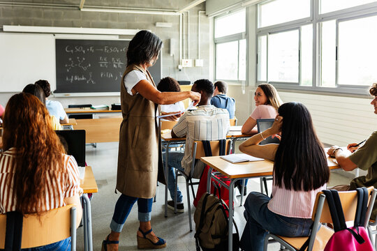 Teacher handing out exams to students during a high school lesson. Diverse classmates sitting quietly at desks while waiting to begin an academic test. Education and assessment concept.