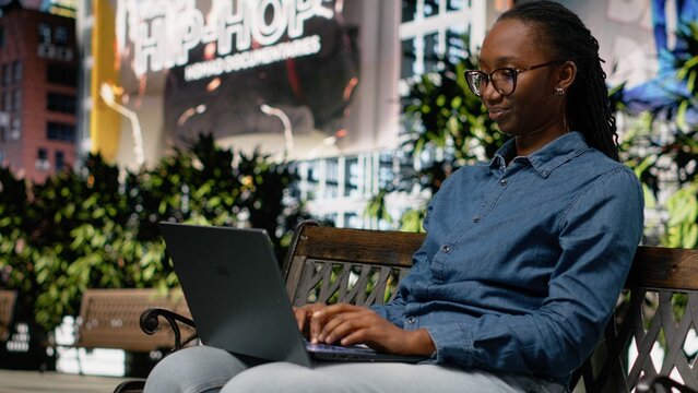 African American woman closes her laptop and leaves the park after finishing work tasks ending her workday in a downtown metropolitan setting.