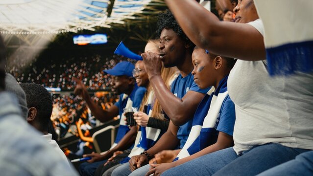 Black mother applies blue face paint to a young child supporter during a live football match as the family enjoys tournament fandom and stadium cheering.