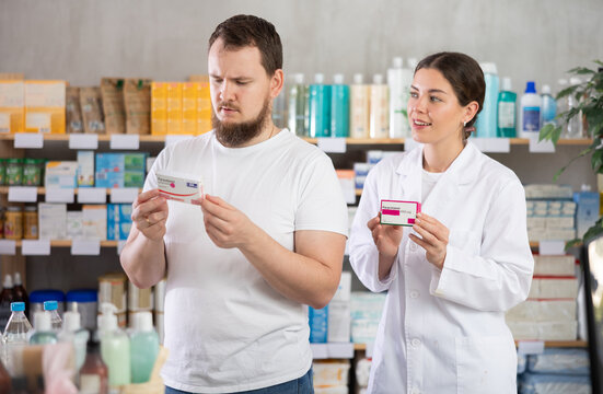 Man chooses paracetamol pills in modern pharmacy. Female pharmacist helps with choosing a medicine
