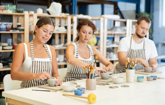 Three pottery workers mold clay into homemade plates and other utensils.