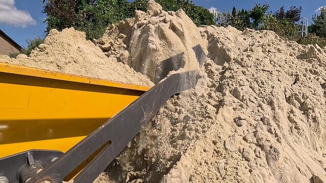 Small excavator loads itself with sand on construction site. Mini dumper transports sand close-up. Tractor loads sandy soil for construction work. Worker uses construction machinery to build house