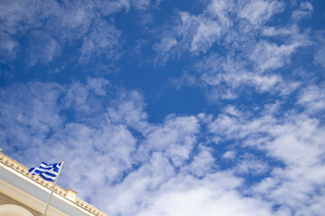 Greek flag flying above a classical building in Zante Greece with a dramatic expanse of blue sky and textured white clouds creating a strong national and architectural scene © Duncan