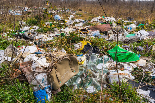 View of an illegal dumping site with scattered household waste, plastic bags, glass jars, and an old handbag discarded in overgrown grass near Lake Varna, Varna, Bulgaria.