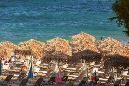 Traditional straw umbrellas and rows of sun loungers on a sandy beach by the Mediterranean Sea in Chania, Crete, Greece.