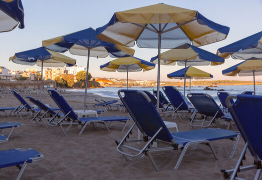 Rows of sun loungers and colorful umbrellas on a sandy beach overlooking the Mediterranean coast in Chania, Crete, Greece.