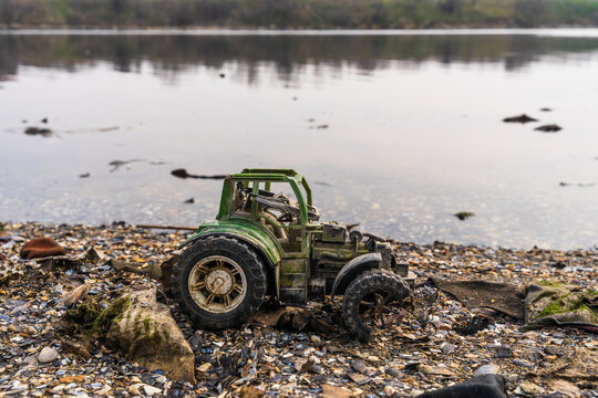 View of a weathered toy tractor abandoned on the pebbly, muddy shore of Lake Varna, Varna, Bulgaria.