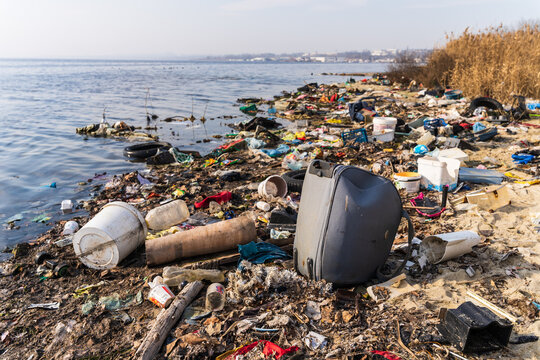 View of Lake Varna shoreline heavily polluted with plastic waste, discarded items, and debris scattered across the sand and water edge, Varna, Bulgaria.