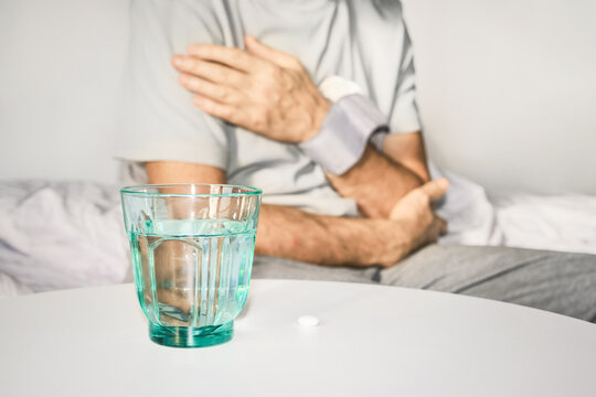 Mature man checking blood pressure at home, medication and glass of water nearby