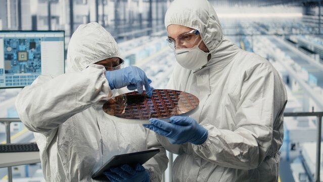 Semiconductor and SOC architecture designers analyze silicon substrates and wafers in a factory while cooperating on microchip quality control in a microelectronics production plant.