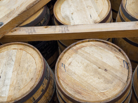 Close view of light oak barrel heads with hand-drawn marks and small stamps, stacked beneath wooden rack beams in a warehouse