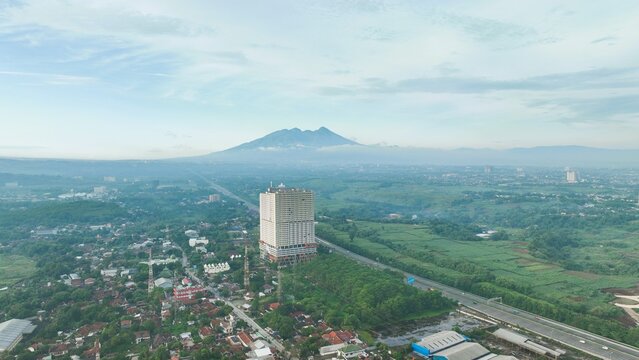 Aerial view of Sentul area featuring a prominent high-rise building, lush green landscapes, and a distant mountain in Babakan Madang, West Java, Indonesia.