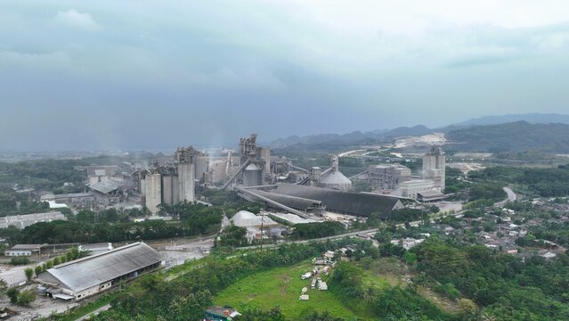 Aerial view of the Nambo cement factory with industrial silos and processing structures surrounded by lush greenery in Klapanunggal, West Java, Indonesia.