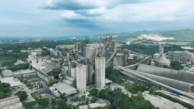 Aerial view of the Nambo cement factory in Klapanunggal, featuring industrial silos, conveyor belts, and processing buildings surrounded by greenery in Klapanunggal, West Java, Indonesia.