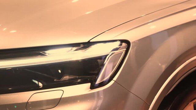 Modern car headlight and fender shine under warm showroom light