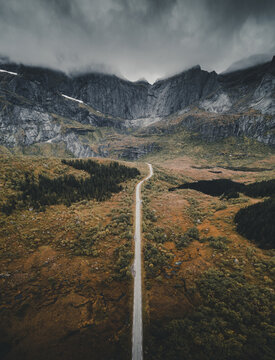 Aerial view of the dramatic Batman wall mountain formation towering over a winding road through the autumn-colored landscape of Ramberg, Nordland, Norway.