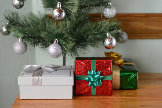 Decorated christmas tree branches holding silver ornaments with colorful wrapped presents placed underneath on wooden table