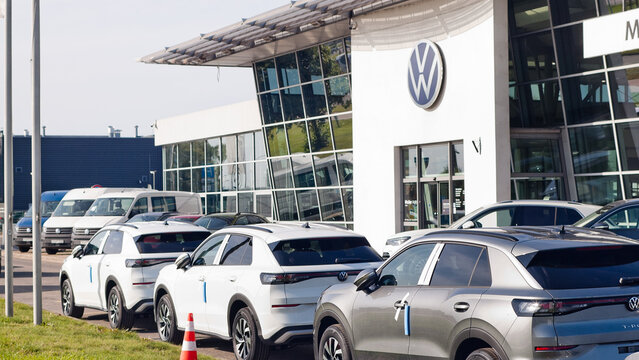Riga, Latvia, August 14, 2026: New Volkswagen cars on the street near the auto center, in the background is the building of the auto center and a billboard with the VW logo
