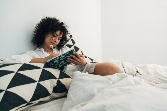 Woman writing journal in bed relaxing morning