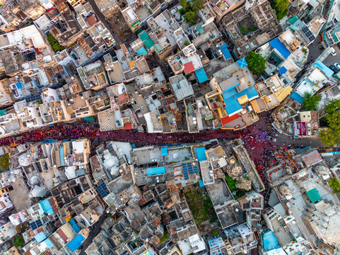 Aerial view of the dense urban landscape of Udaipur with narrow streets filled with colorful festival activity, traditional rooftops, and varied architecture in Udaipur, Rajasthan, India.