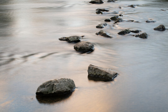 Rocks lie in the river, forming a natural crossing. The water flows slowly past the rocks.