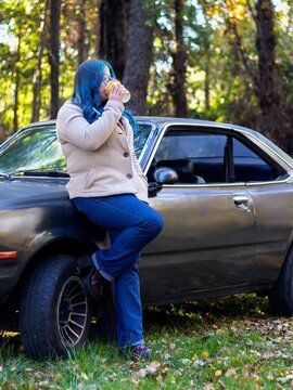 Woman with blue hair drinking coffee beside car