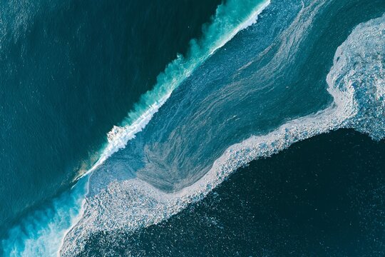 Ocean wave crashes over swirling masses of plastic debris. Sea pollution accumulates along the water surface, creating a visible line. Environmental crisis highlights damage to marine ecosystems