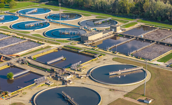 Aerial view of circular settling tanks and aeration basins at a large wastewater treatment facility in Italy.