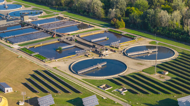 Aerial view of circular clarifiers, treatment basins and solar panel arrays at a modern wastewater treatment facility in Italy.