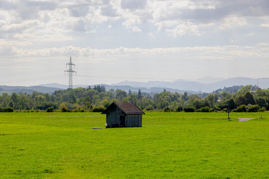 Bavarian countryside landscape, A traditional wooden barns standing alone on a rolling hill, Lush green grass meadow against majestic Alpine mountains under blue sky and white clouds, Bavaria, Germany