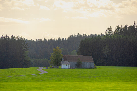 Bavarian countryside landscape, A traditional wooden barns standing alone on a rolling hill, Lush green grass meadow against majestic Alpine mountains under blue sky and white clouds, Bavaria, Germany