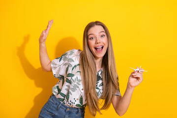 Cheerful young woman holding a paper plane smiling joyfully on a bright yellow background
