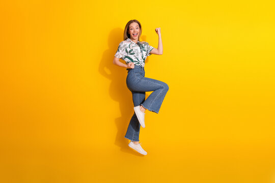 Cheerful young woman in fashionable casual attire jumping with joy on yellow background showcasing vibrant lifestyle