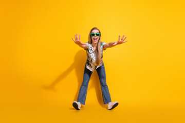 Cheerful young woman with sunglass striking a fun pose in a vibrant outfit against a bright yellow background © deagreez