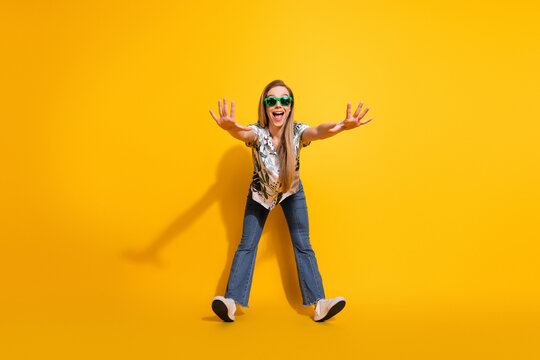 Cheerful young woman with sunglass striking a fun pose in a vibrant outfit against a bright yellow background