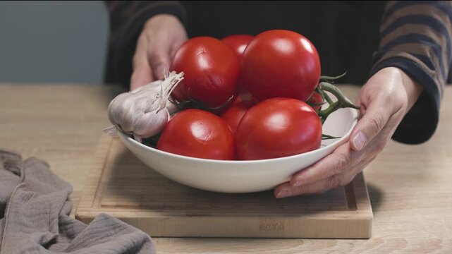 chef places  bowl of fresh tomatoes and garlic on a wooden kitchen table to prepare a healthy meal, food closeup. Ingredients for tomato pasta